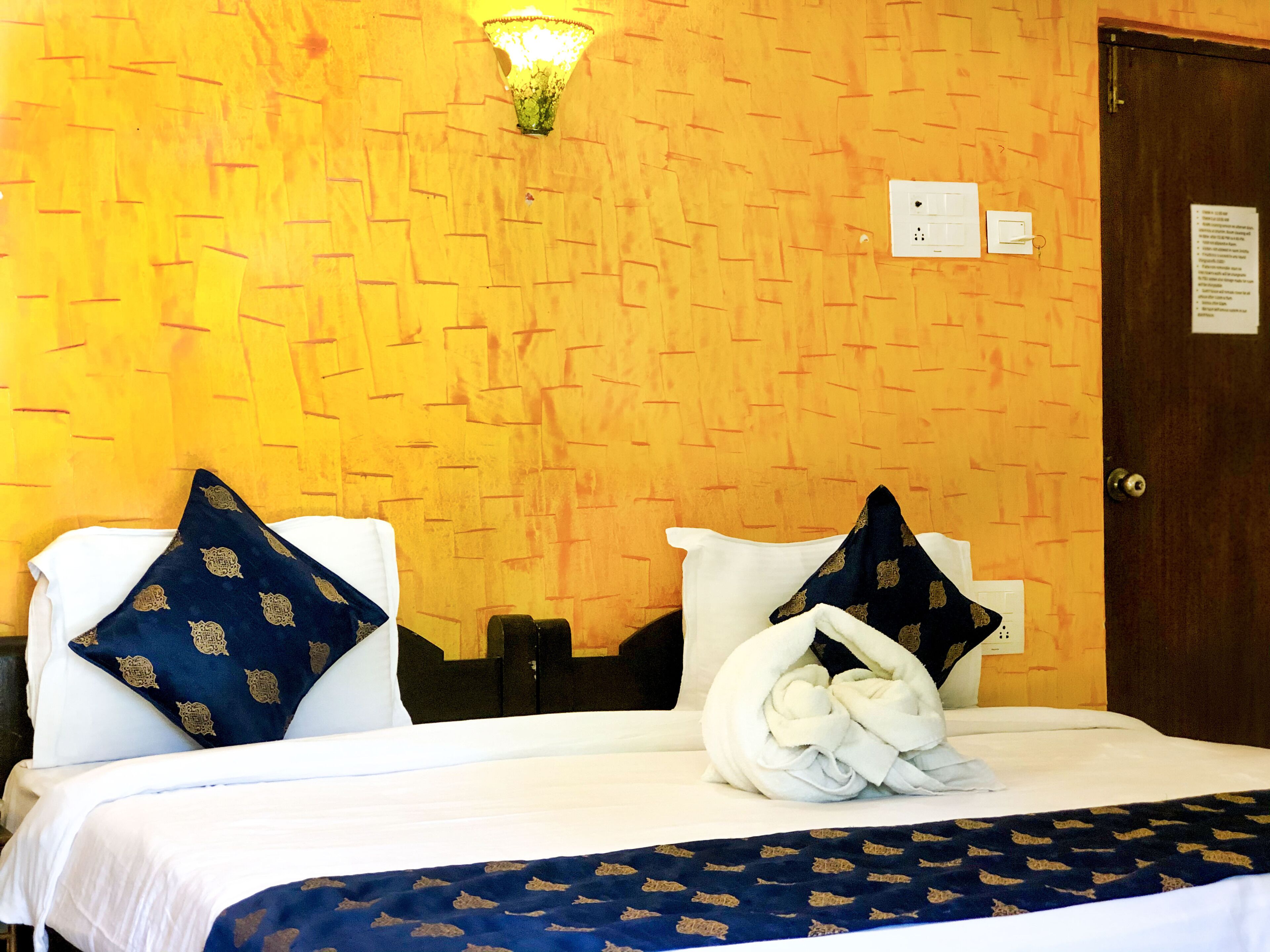 A hotel room with a bed, two pillows, a wall-mounted light, and a door.