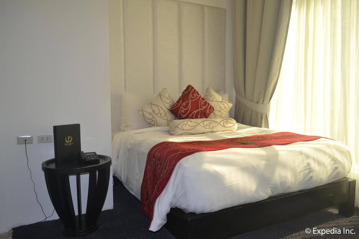 A neatly made bed with white bedding and a red throw, a bedside table with a phone and a book, and a power outlet on the wall.