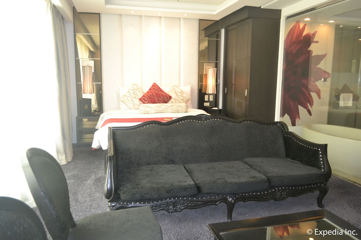 A hotel room with a large bed, a dark upholstered sofa, a glass coffee table, and a large mirror.