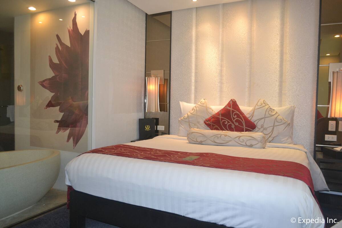 A hotel room with a large bed, a red and white bedspread, and a wall-mounted mirror.