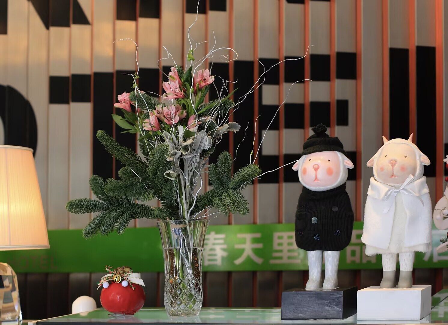 Een hotel receptie met een bloevas, een lamp en twee beeldjes op een tafel.