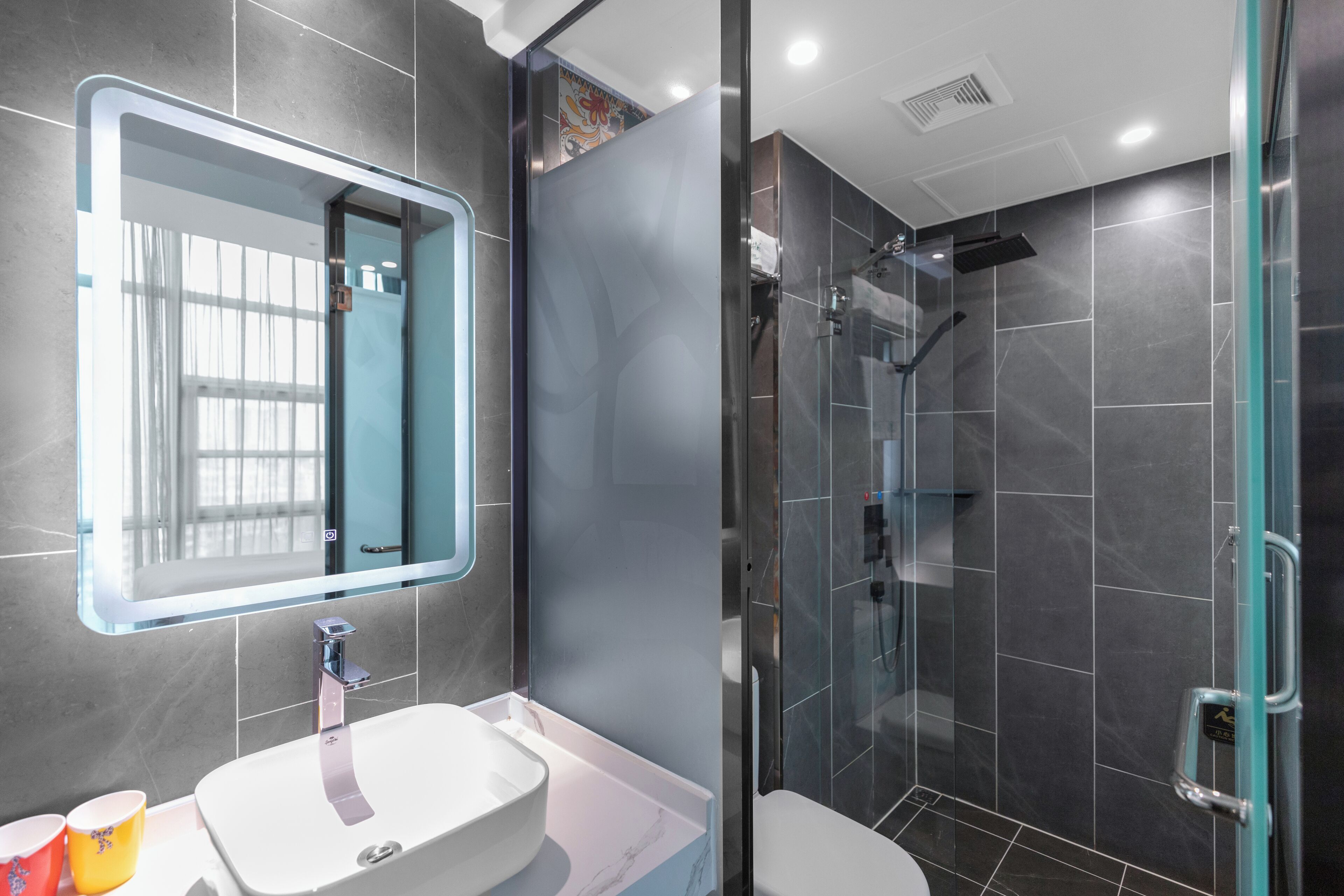 A modern bathroom with a large mirror, a white sink, and a glass-enclosed shower area.