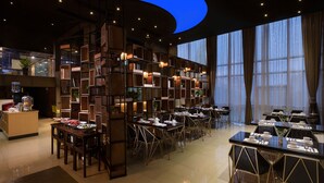 A modern hotel dining area with multiple tables, a central bookshelf, and large windows. - Spring Time Hotel (Guangzhou)
