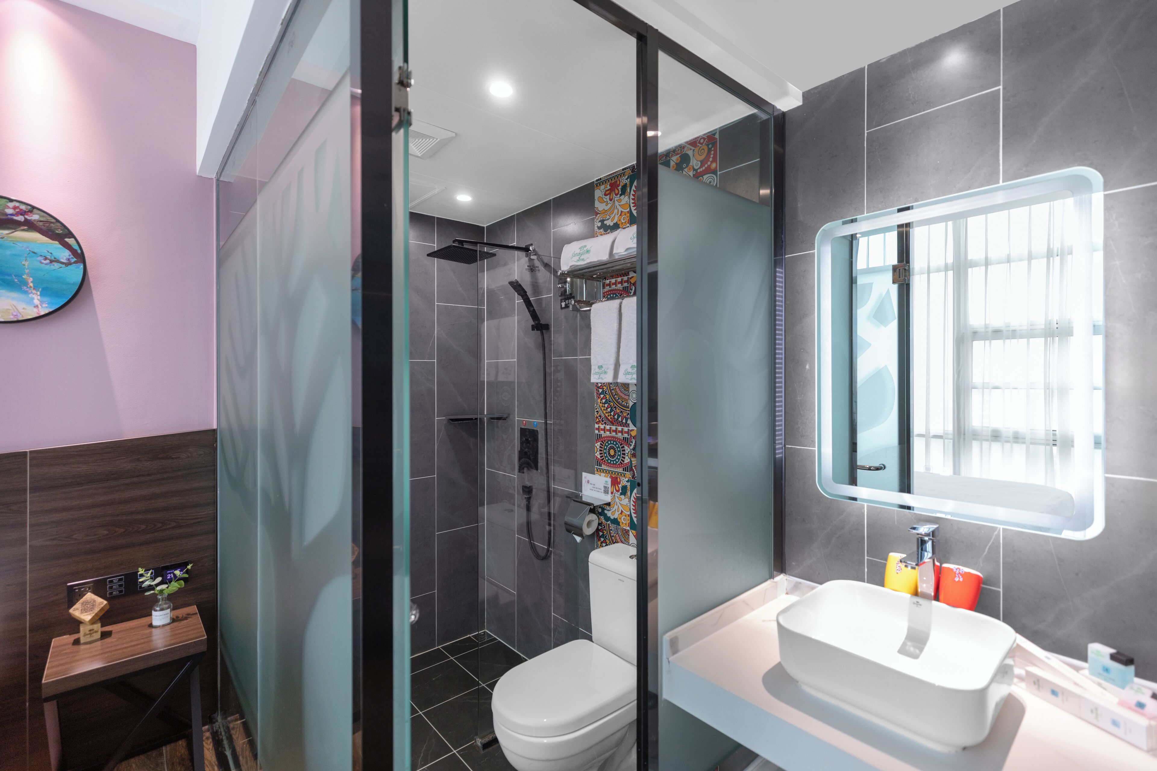 Een moderne badkamer met een glazen douchecabine, een wit toilet en een grote spiegel boven een witte wastafel.