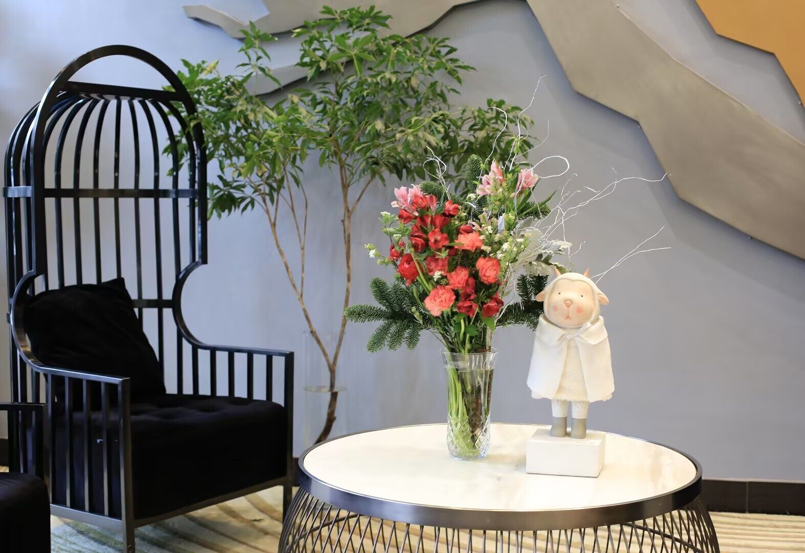 A round table with a vase of flowers and a decorative sheep figure.