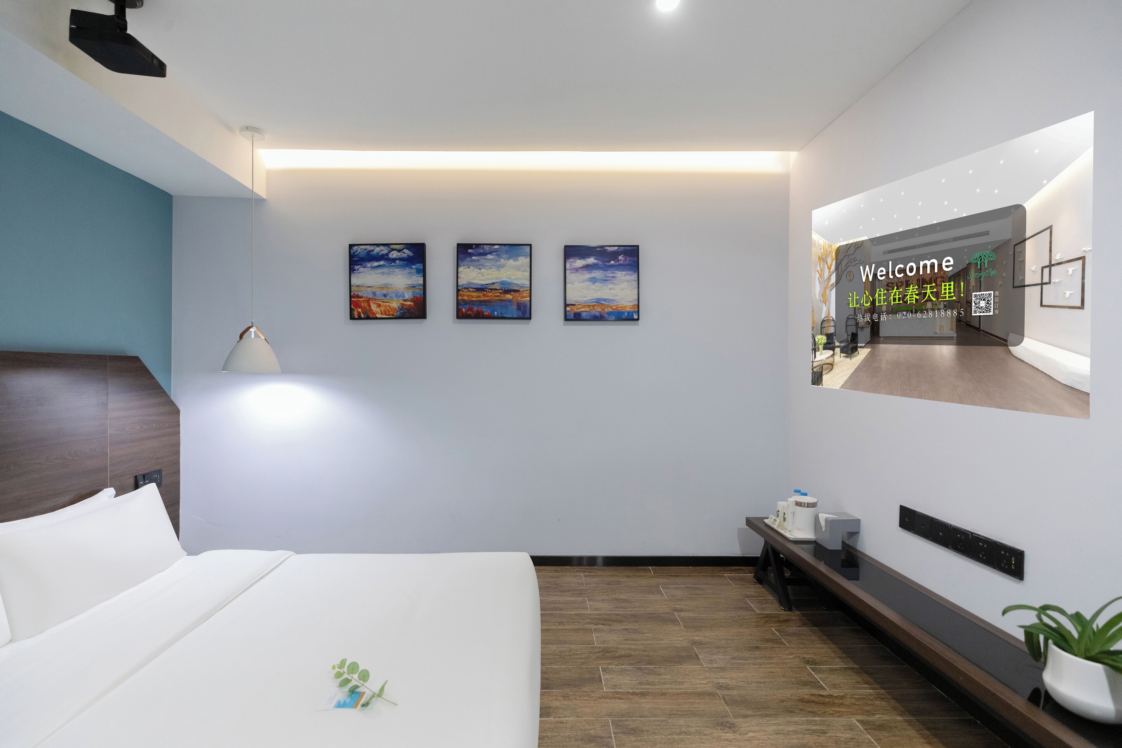 A modern hotel room with a large bed, a bedside table, a nightstand, a wall-mounted TV, and three landscape paintings.