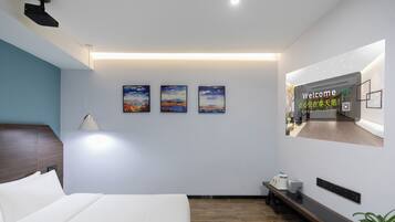 A modern hotel room with a large bed, a bedside table, a nightstand, a wall-mounted TV, and three landscape paintings.