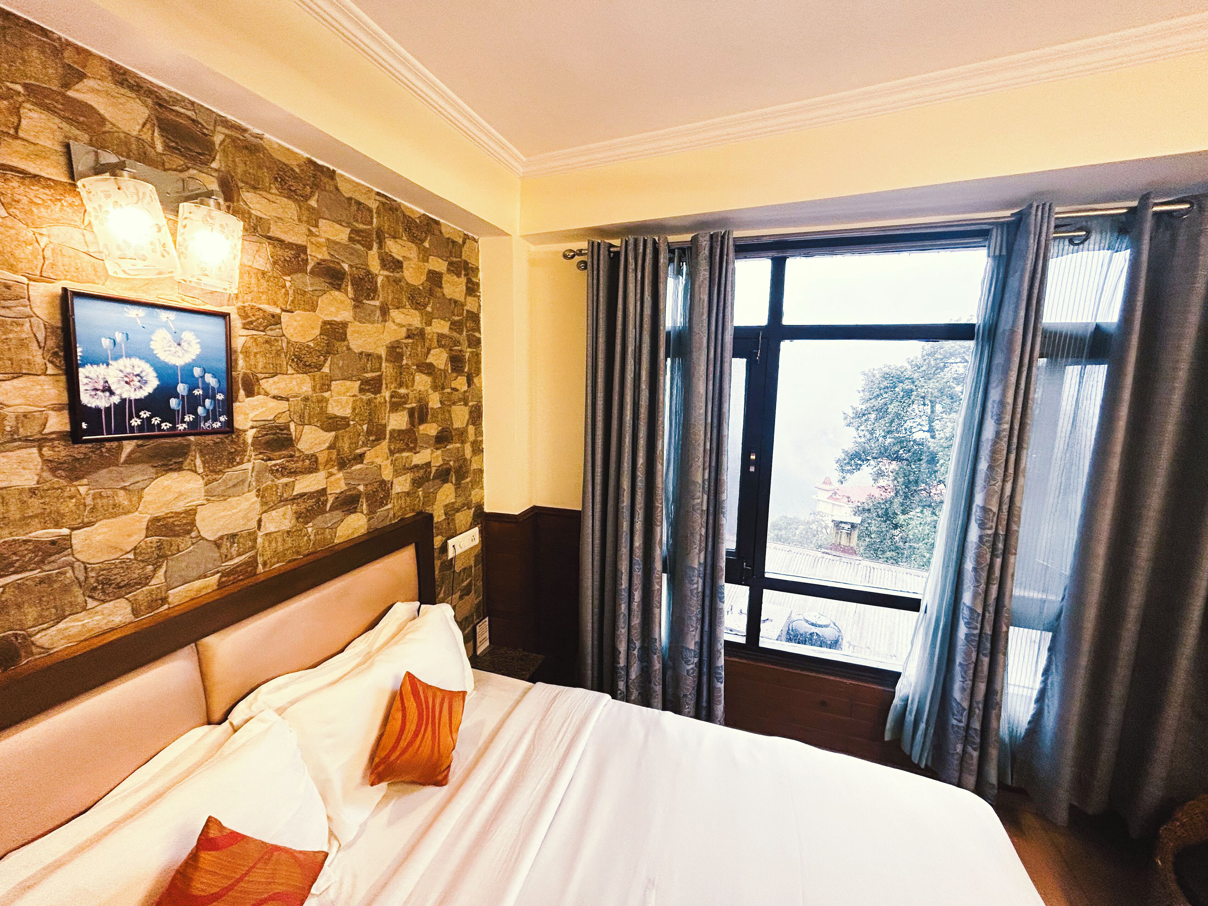 A hotel room with a stone wall, a bed with white bedding, a framed picture, and a window with curtains.