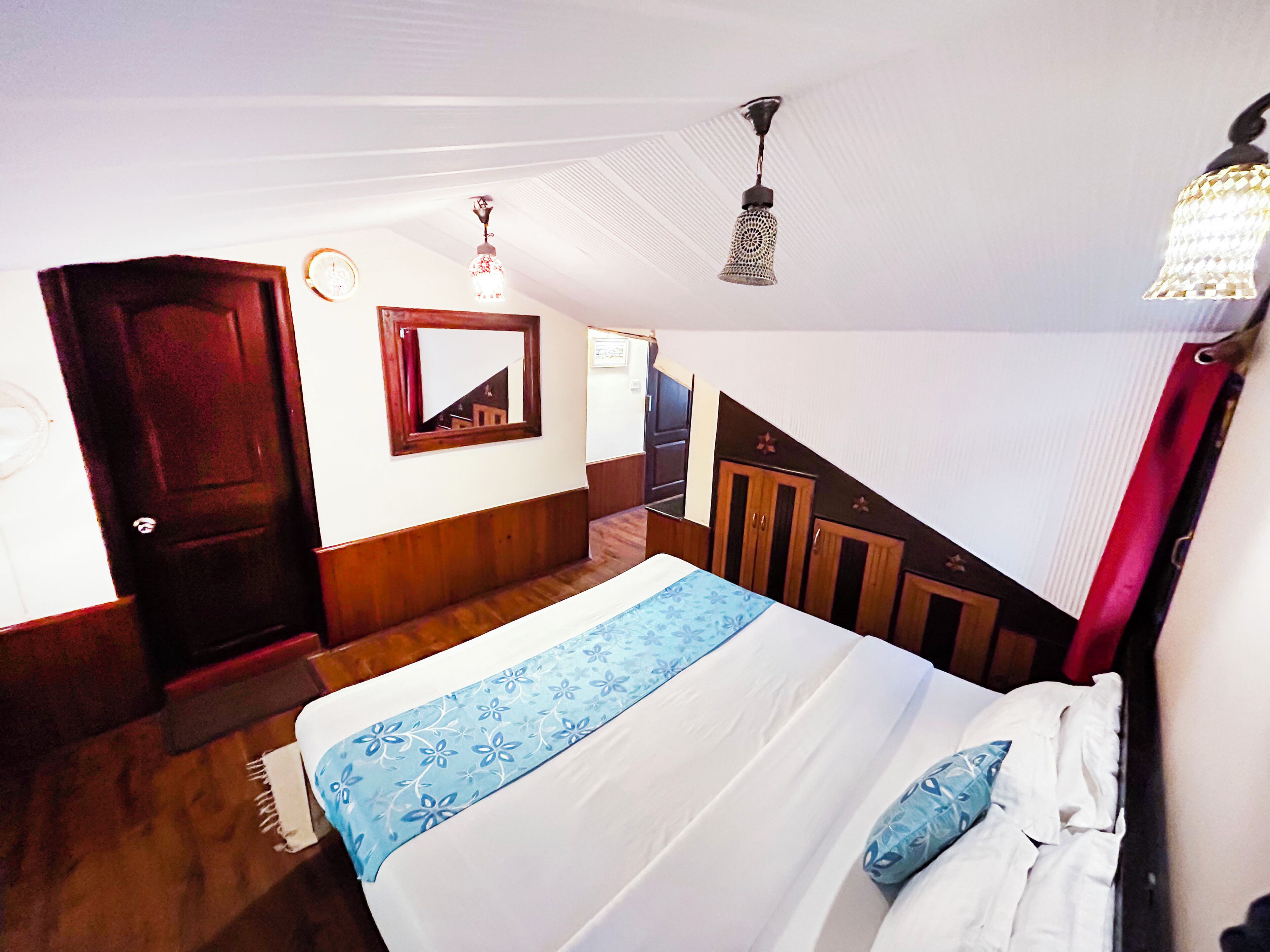 A bedroom with a bed, wooden wardrobe, a mirror, and a staircase.