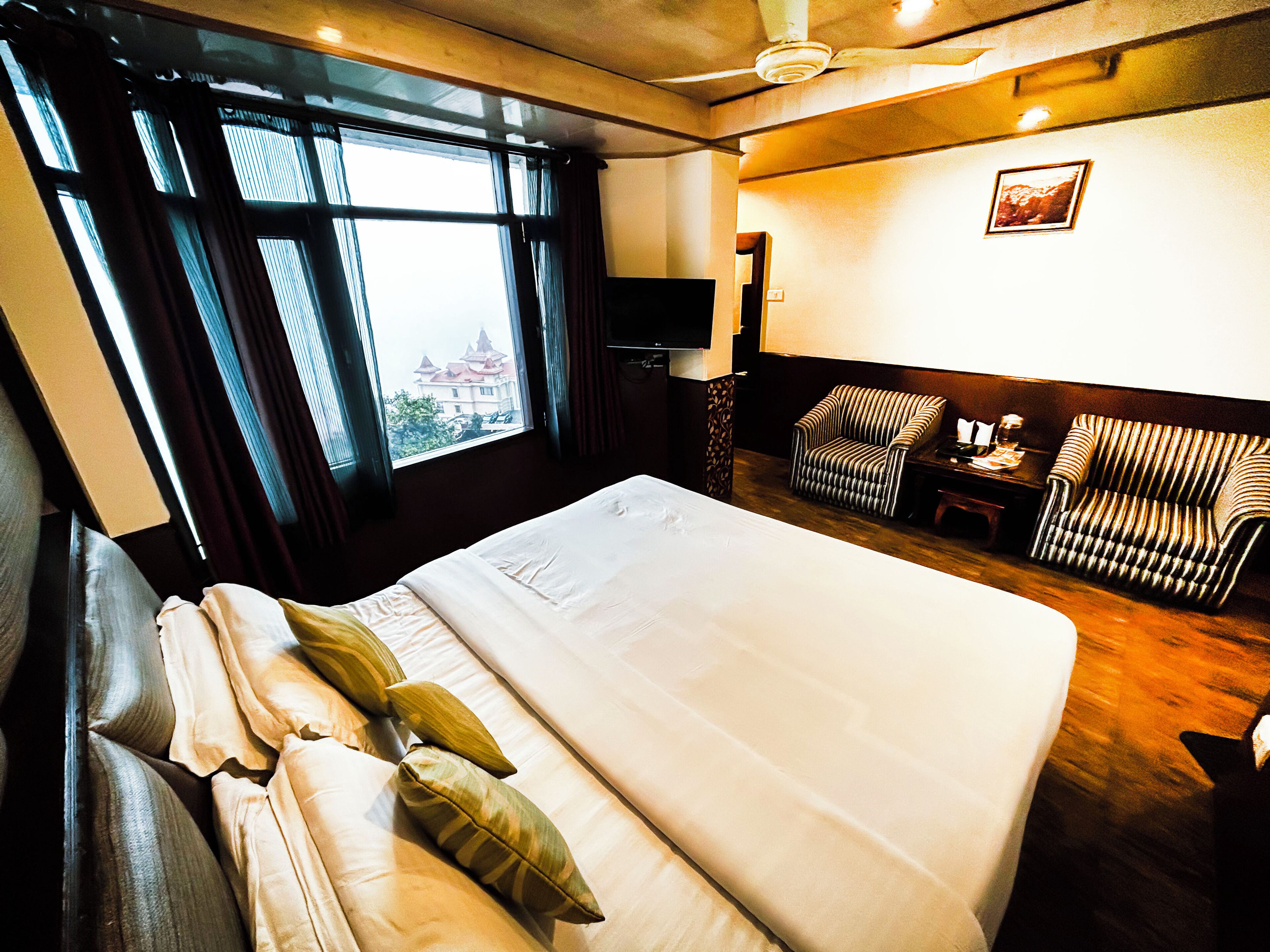 Hotellihuone, jossa on suuri sänky, tuoli, työpöytä ja ikkunasta avautuva näkymä rakennukseen.