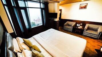 Hotellihuone, jossa on suuri sänky, tuoli, työpöytä ja ikkunasta avautuva näkymä rakennukseen.