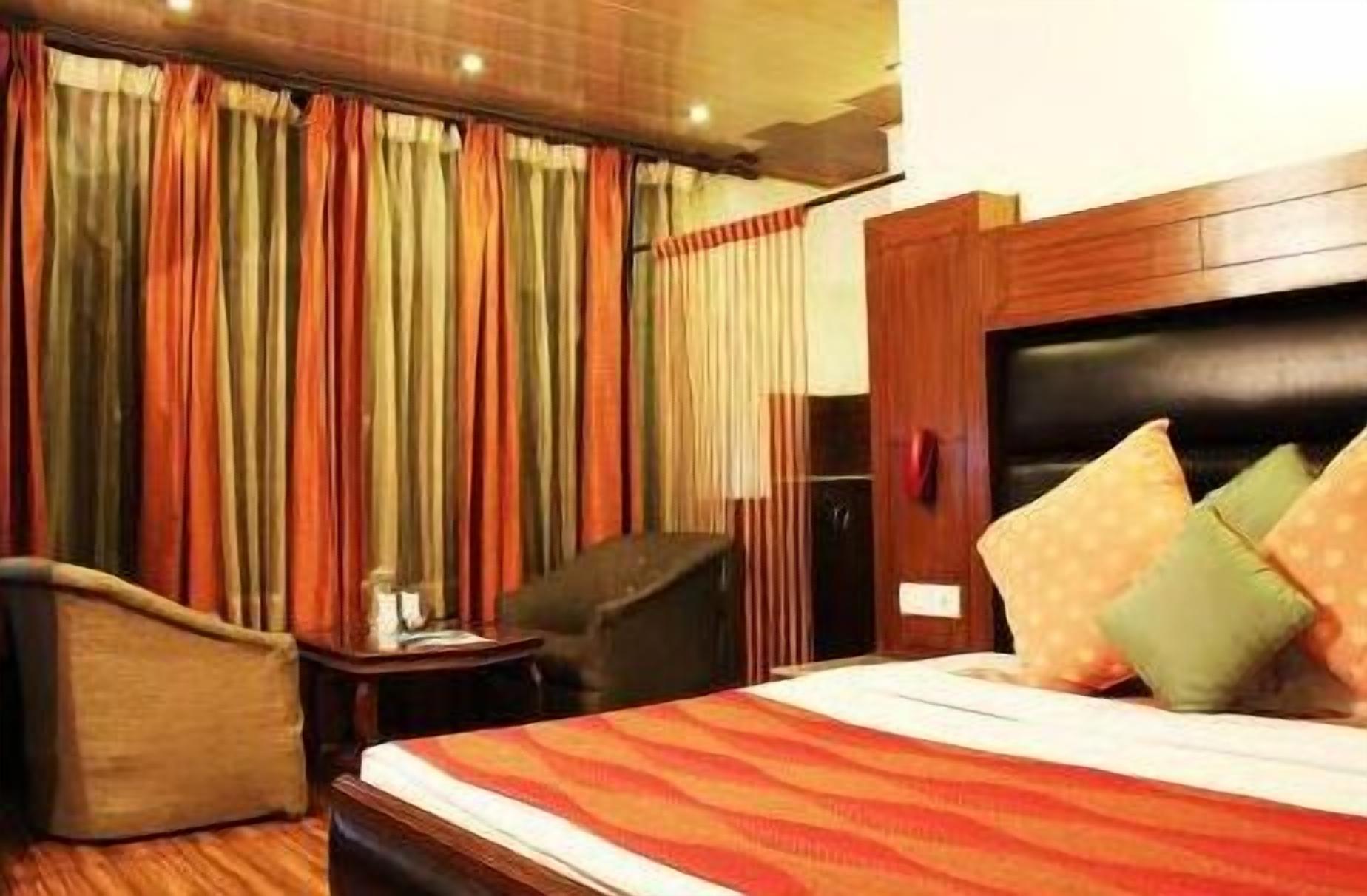 Una habitación de hotel con una cama, una silla, una mesita de noche y cortinas.