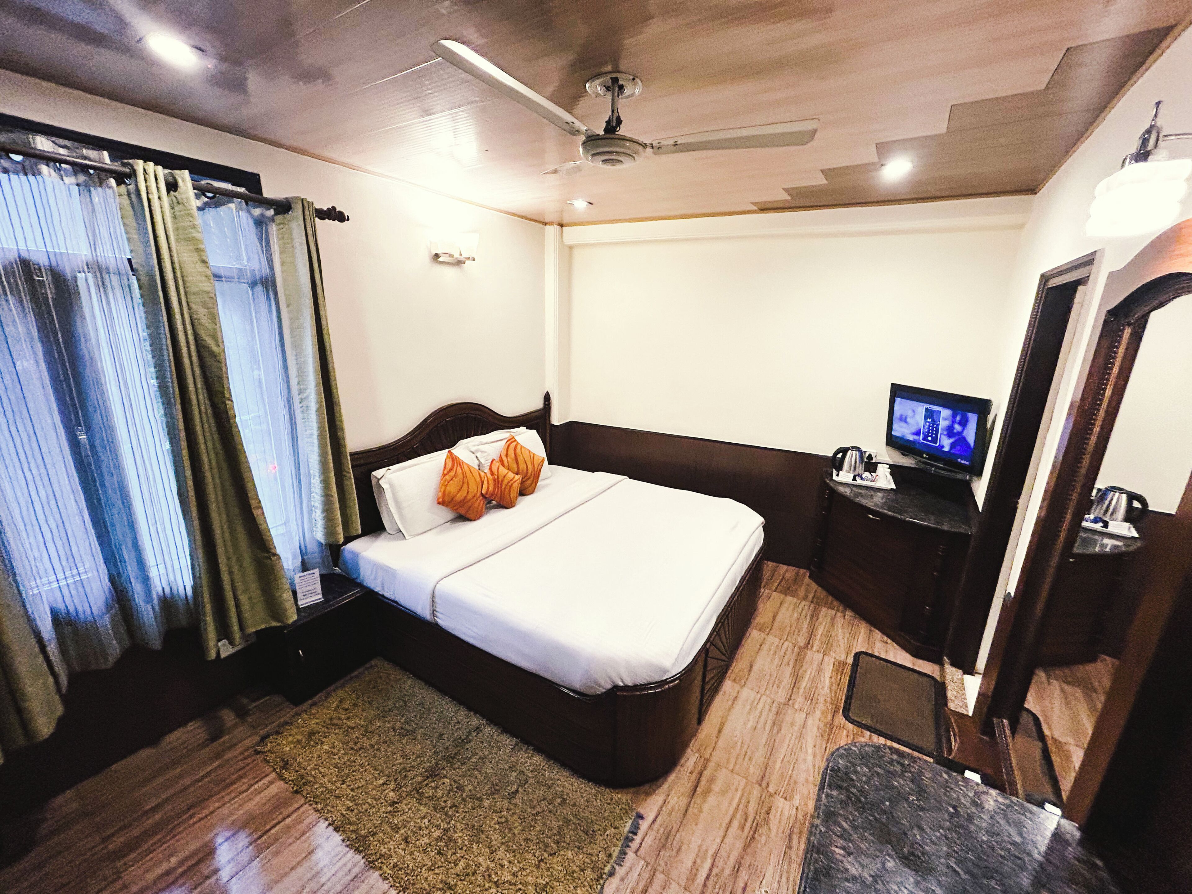 A hotel room with a bed, a television, a mirror, and a ceiling fan.