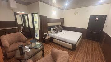 Una habitación de hotel con cama, dos sillones, una mesita, una mesita de noche, un espejo y un armario.