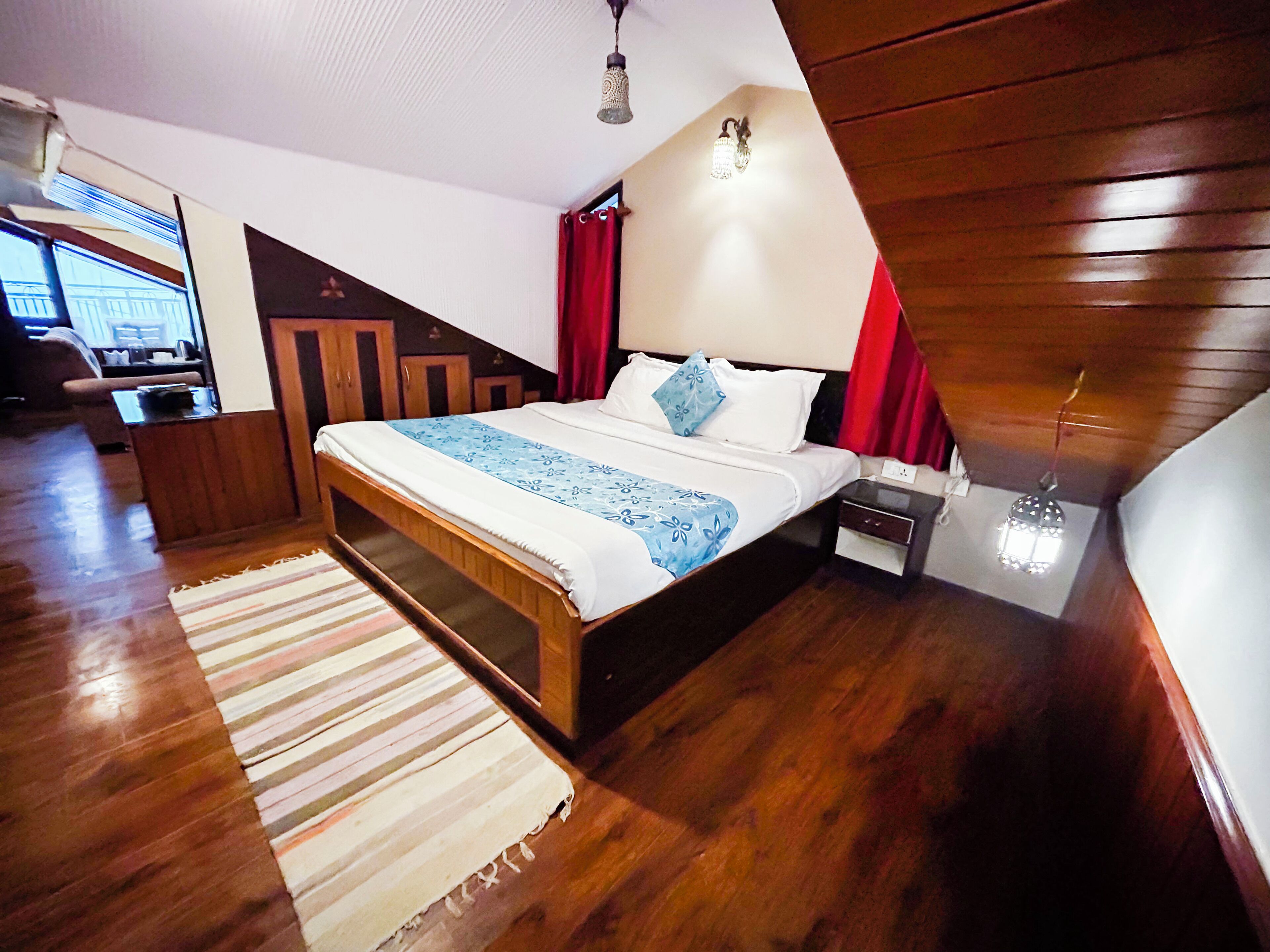 A bedroom with a wooden bed, a nightstand, a lamp, and a window with curtains.