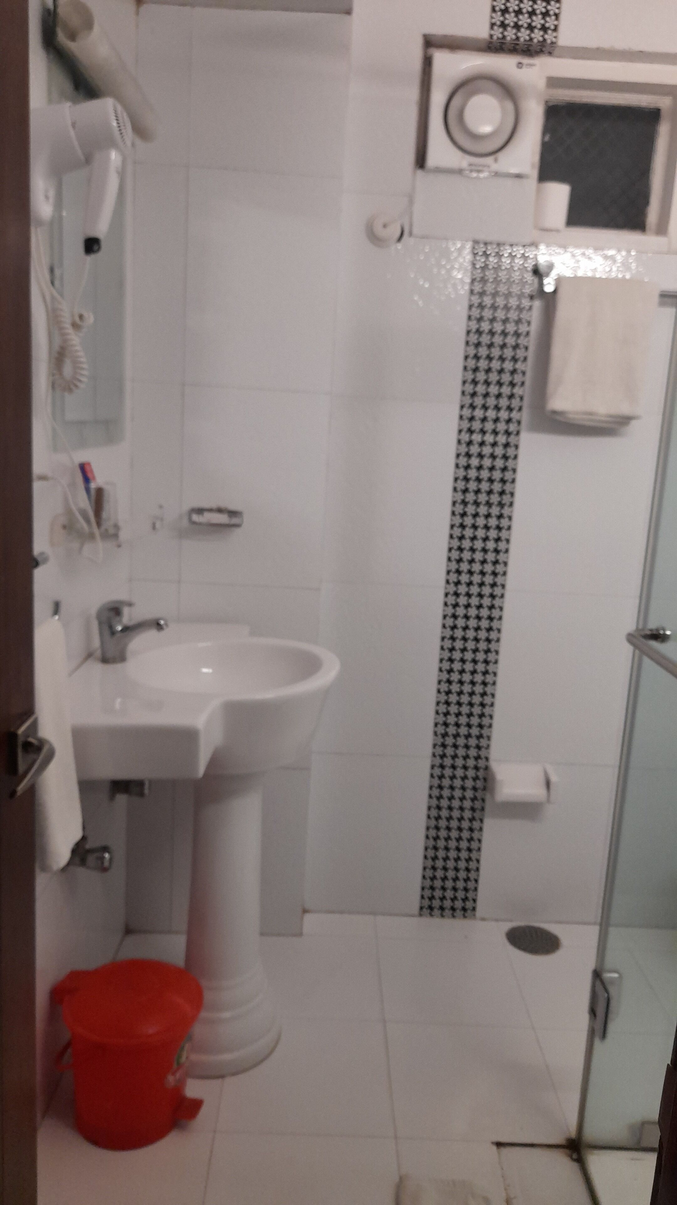 A bathroom with a white sink, a red trash bin, a shower area, and a patterned wall.