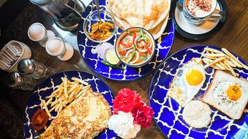 Una mesa de desayuno con diversos platos, incluyendo huevos, panqueques y papas fritas, sobre fuentes azules decorativas.
