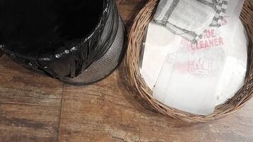 A black trash bin and a wicker basket with a white bag labeled "STORAGE CLEANER" on a wooden floor.