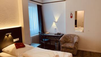 Ein Hotelzimmer mit Bett, Schreibtisch, Stuhl, Heizkörper und einem fenster mit Vorhängen.