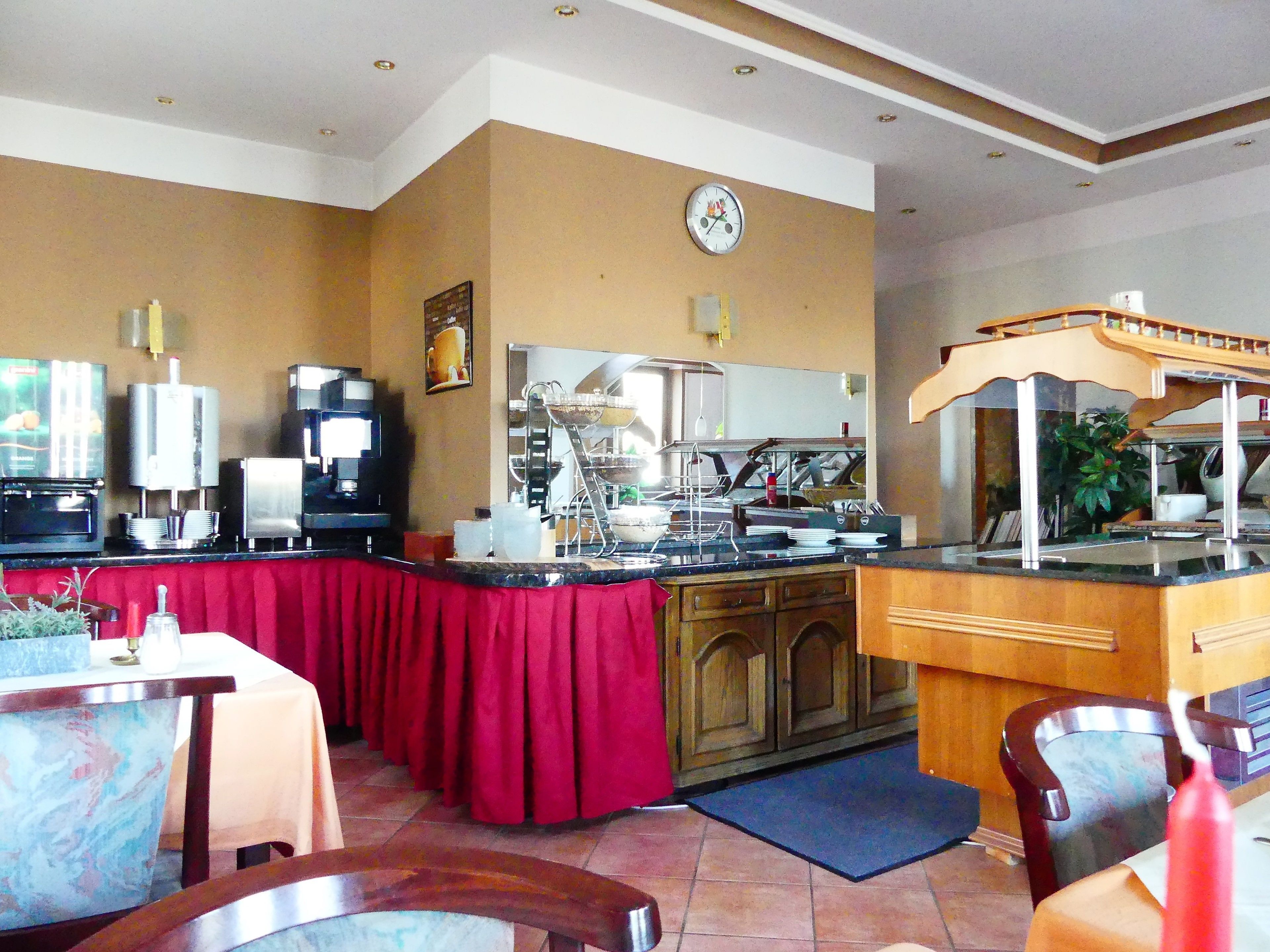 A restaurant with a red tablecloth, a coffee machine, and a clock on the wall.
