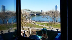 A view of a river with a bridge, trees, and people in a park. - Kunibert der Fiese (Cologne)