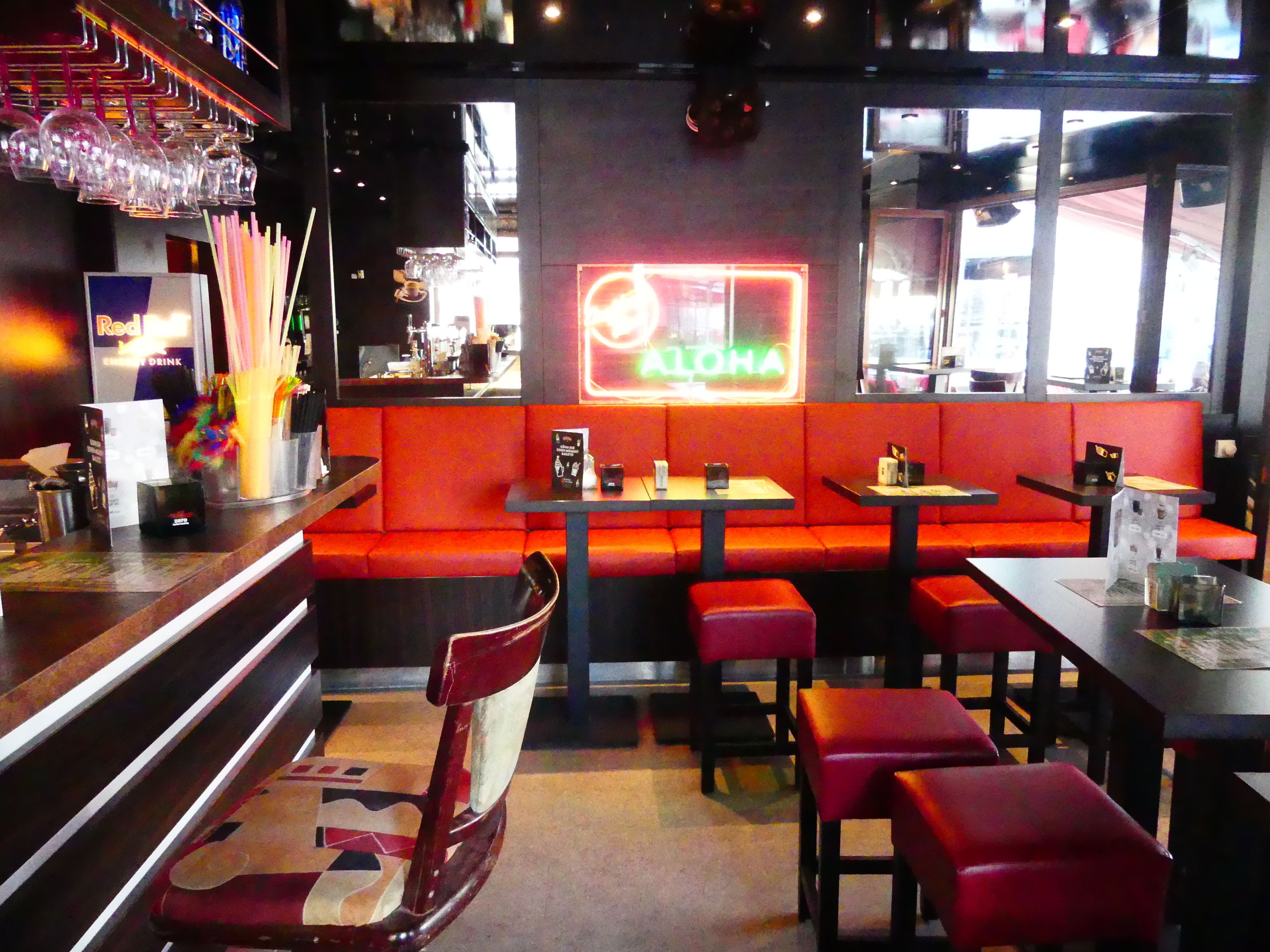 A restaurant interior with red seating, a neon sign, and a bar area with glasses and utensils.
