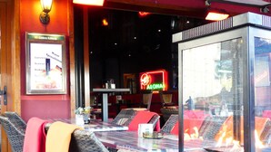 A restaurant interior with wicker furniture, a glass partition, and a neon sign. - Kunibert der Fiese (Cologne)