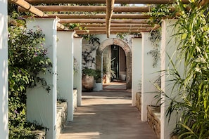 A covered walkway with white walls and arches, leading to a door. - Tenuta del Poggio Antico (Forio)