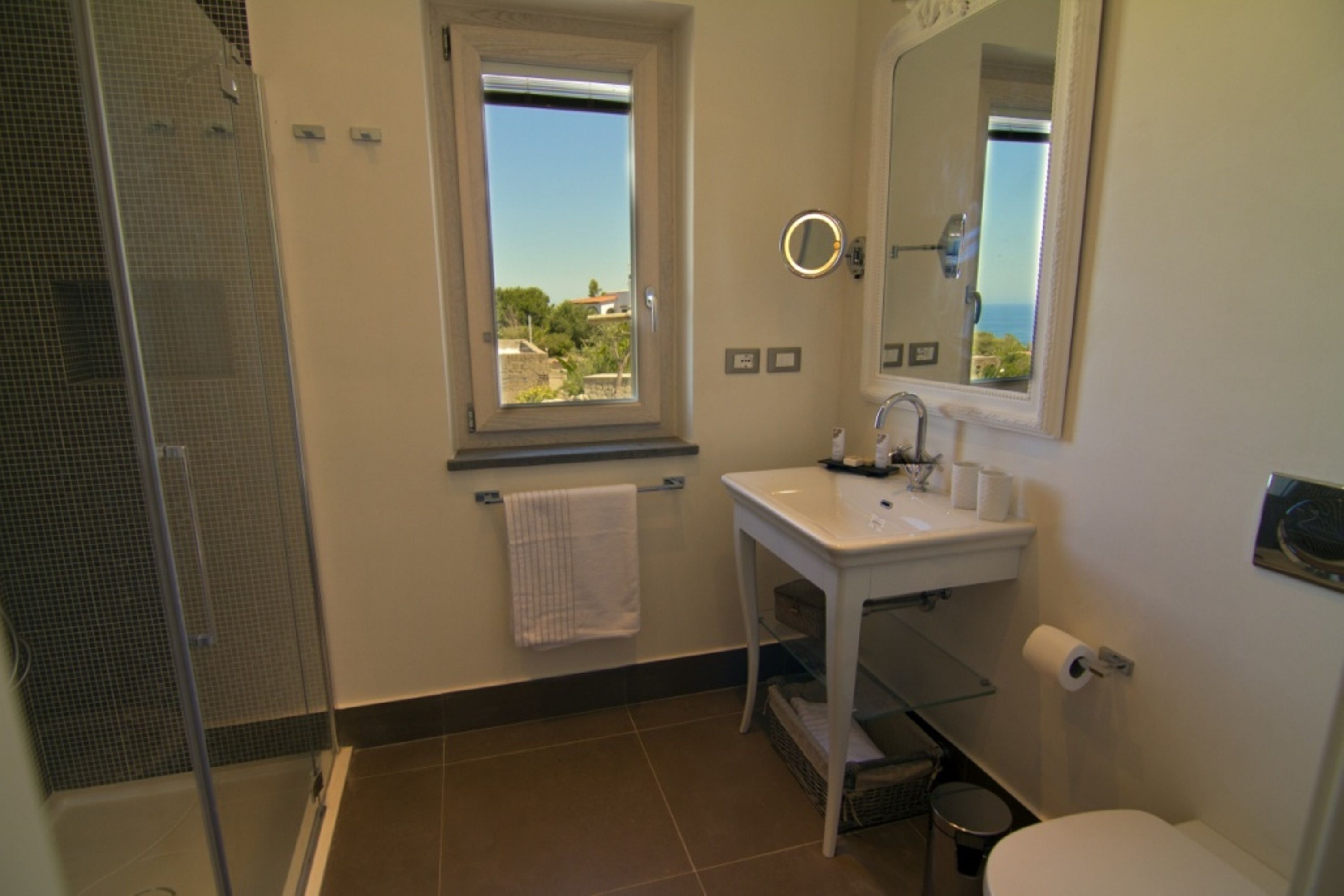 Un baño con ducha, lavabo, inodoro y ventana con vistas.