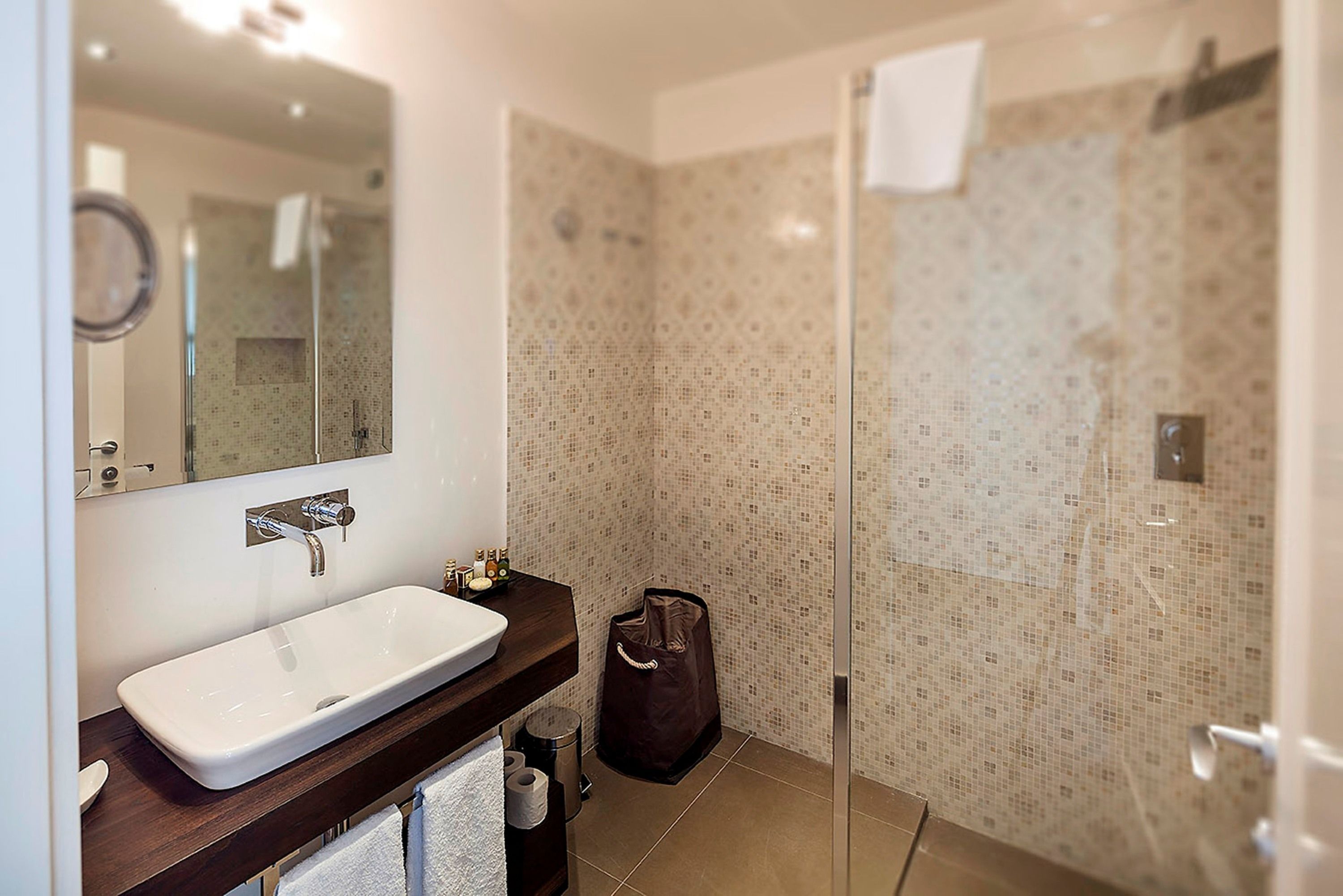 Un baño con un lavamanos blanco, un espejo y una ducha con azulejos estampados.