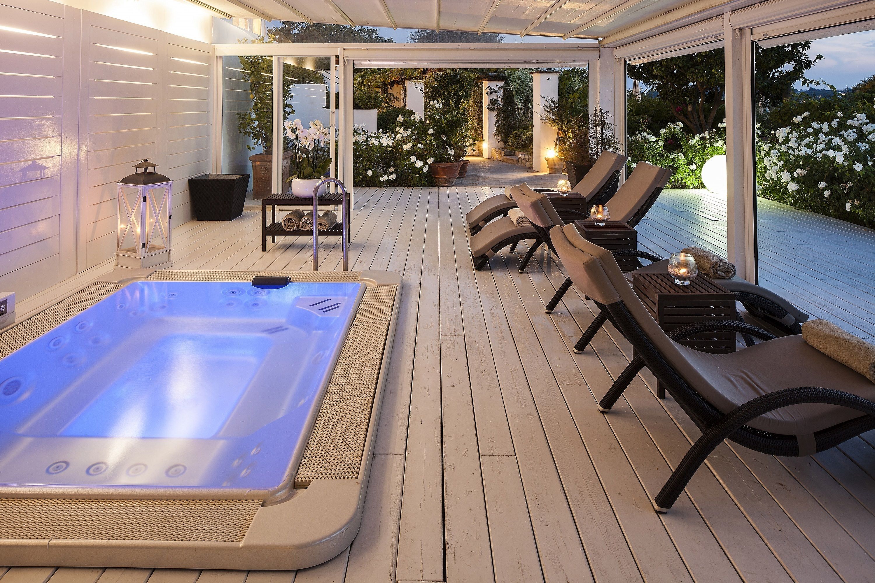 A covered outdoor area with a hot tub, lounge chairs, and potted plants.