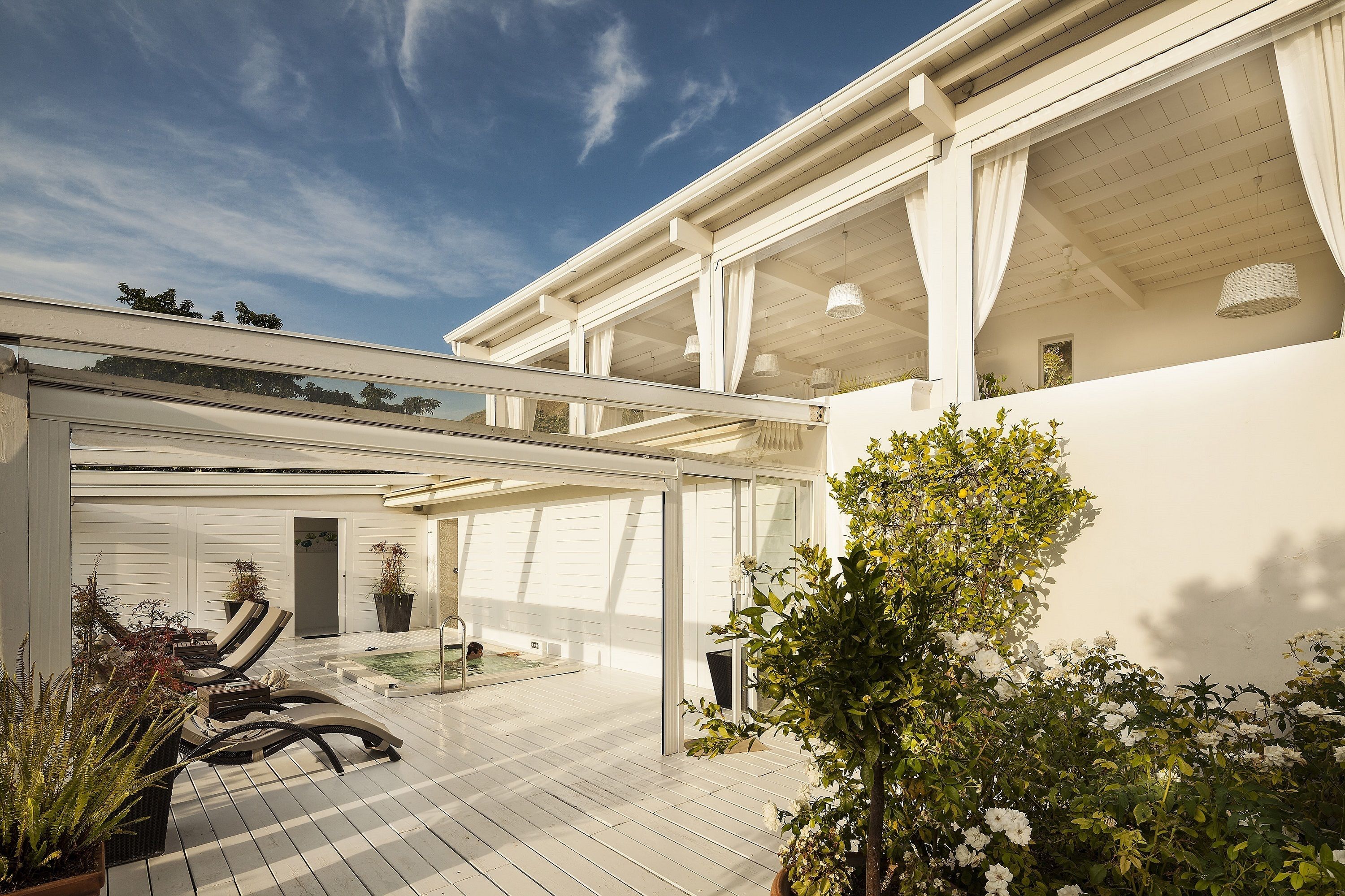 Une terrasse couverte, aménagée avec du mobilier d’extérieur, une piscine et des plantes en pot.