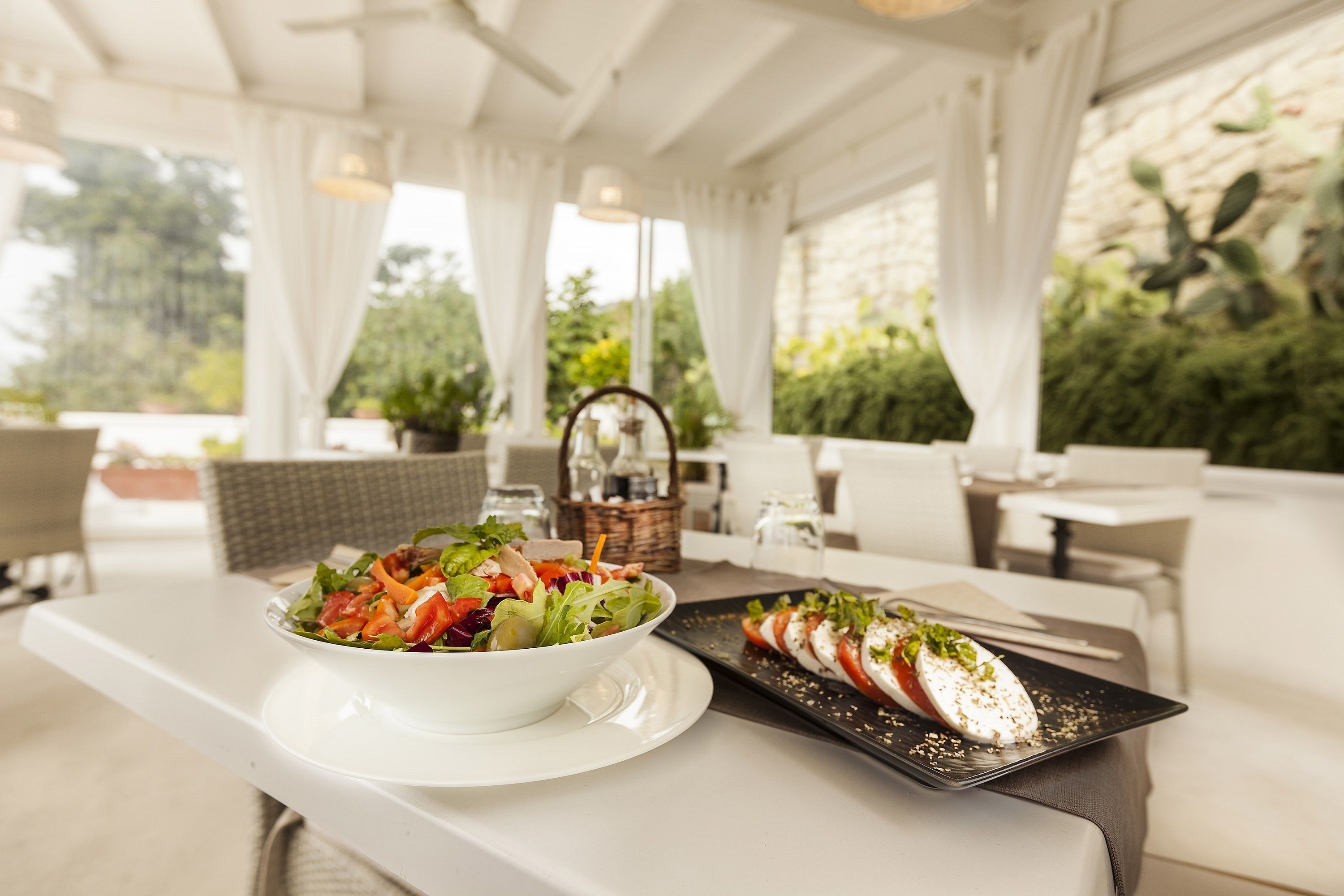 Una mesa de comedor con un plato blanco de ensalada y un plato negro con rodajas de tomate y mozzarella.