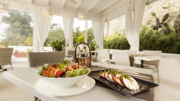 Una mesa de comedor con un plato blanco de ensalada y un plato negro con rodajas de tomate y mozzarella.