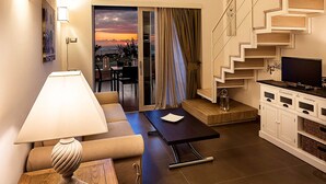 A modern living room with a sofa, a coffee table, a lamp, a TV, and a staircase with a unique design. - Tenuta del Poggio Antico (Forio)
