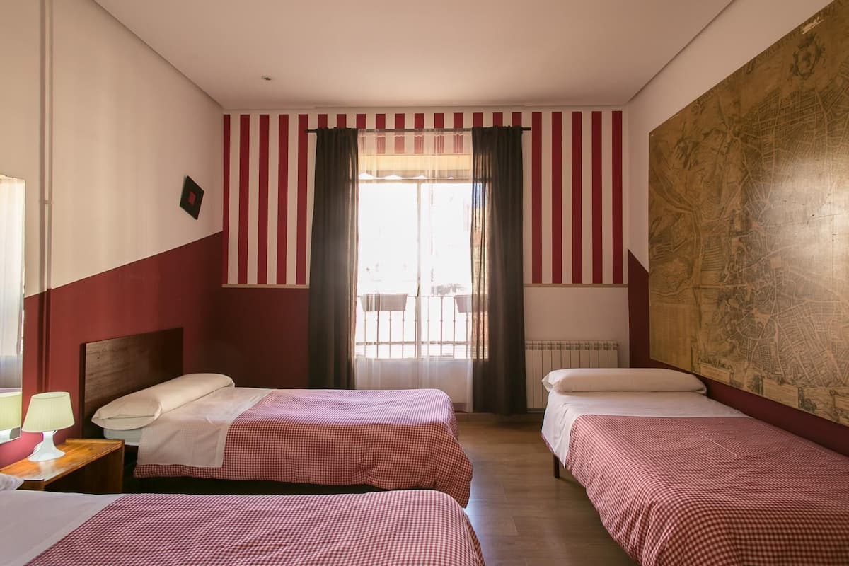 A hotel room with two beds, striped curtains, a map on the wall, and a view of the outside balcony.
