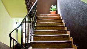 A wooden staircase with a handrail, leading to a landing with a potted plant. - Hostal Abaaly (Madrid)
