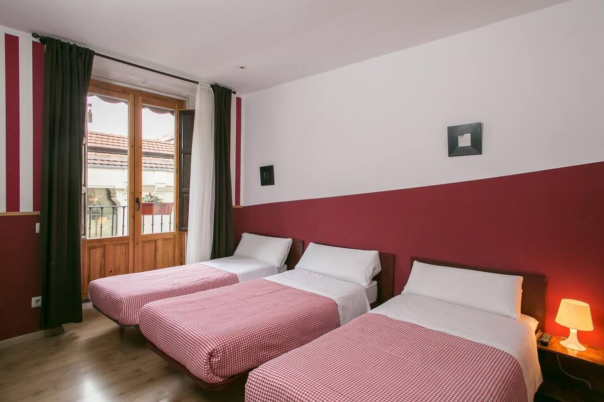 A hotel room with two single beds, a wooden door, a balcony, and a red and white wall color scheme.
