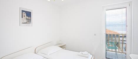Habitación de hotel con dos camas, una mesita de noche pequeña, un cuadro en la pared y un balcón con vistas.