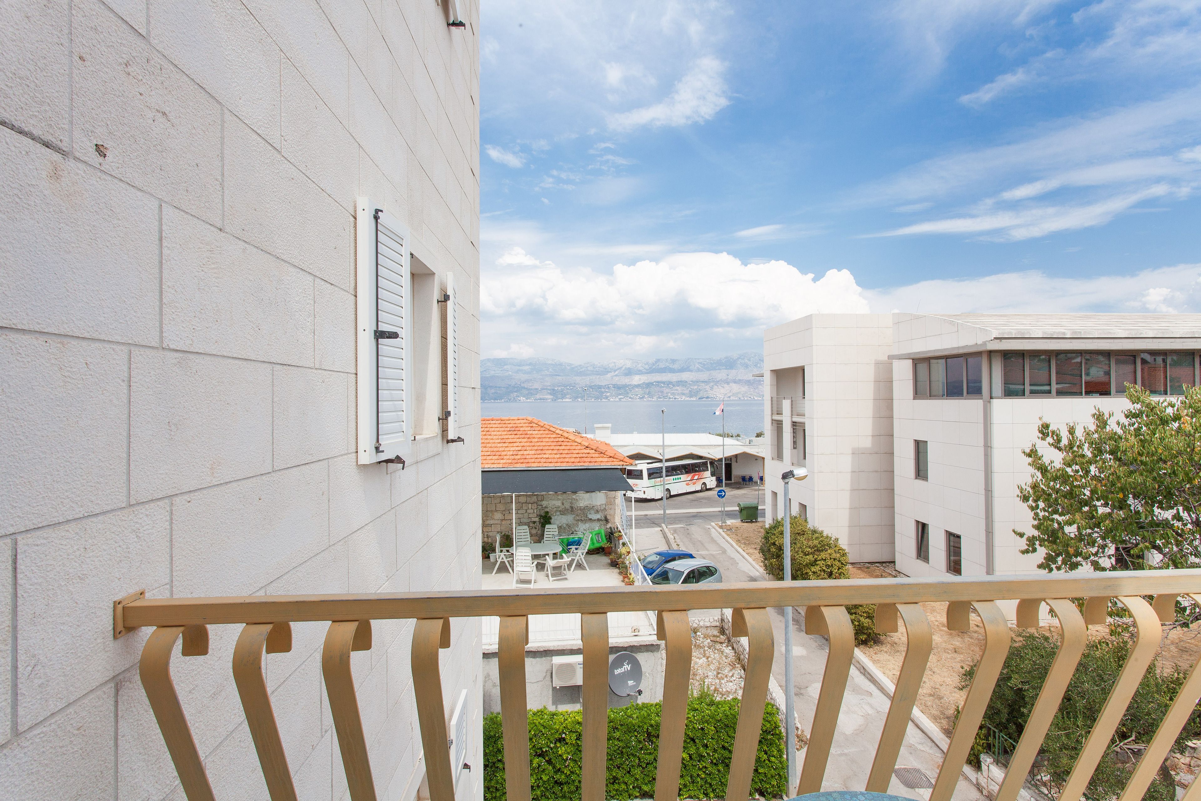 A balcony with a view of a street, a bus, and a building with a tiled roof.