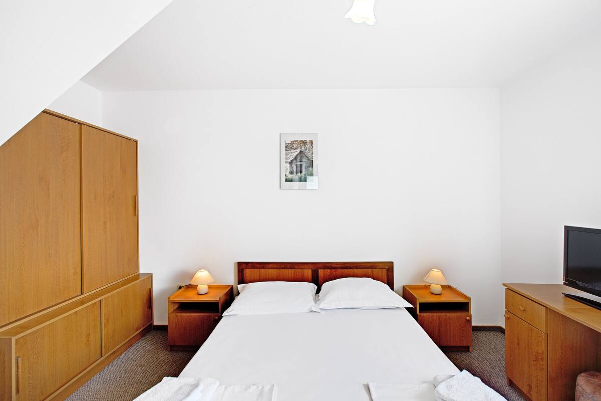 A hotel room with a large bed, wooden wardrobe, bedside tables with lamps, and a television on a wooden cabinet.