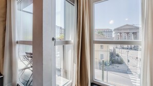 A room with a large window, curtains, and a view of a building with columns. - Hotel Milano Navigli (Milan)