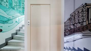 A hallway with a beige elevator, a staircase with a green mural, and a black and white mural on the wall.