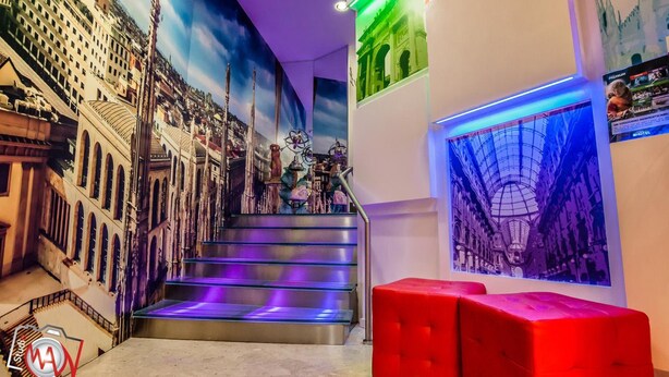 A hotel interior with a staircase leading to a balcony, decorated with cityscape murals and a red seating area. - Hotel Milano Navigli (Milan)
