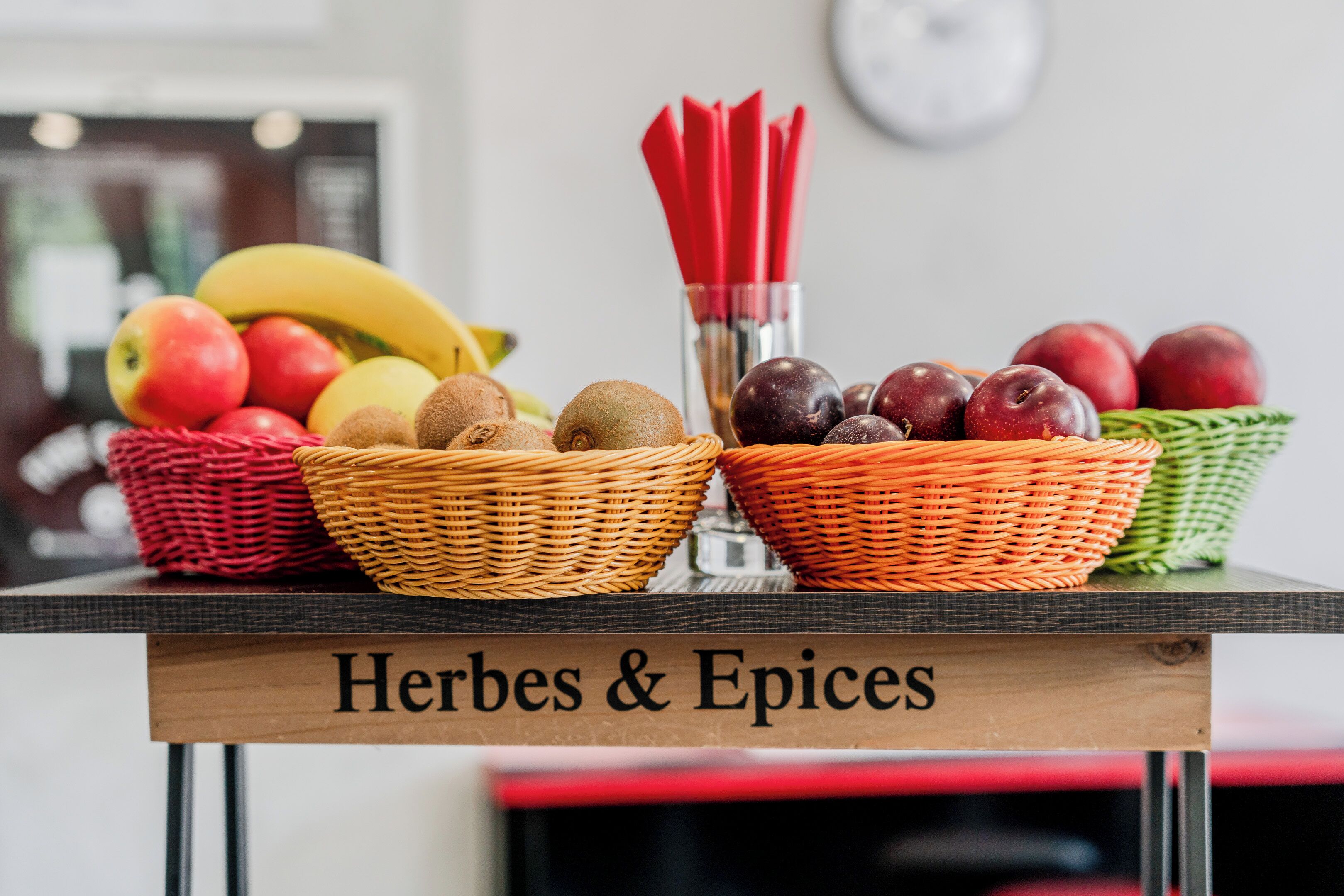 A table with baskets of fruits and a sign reading "Herbes & Epices".