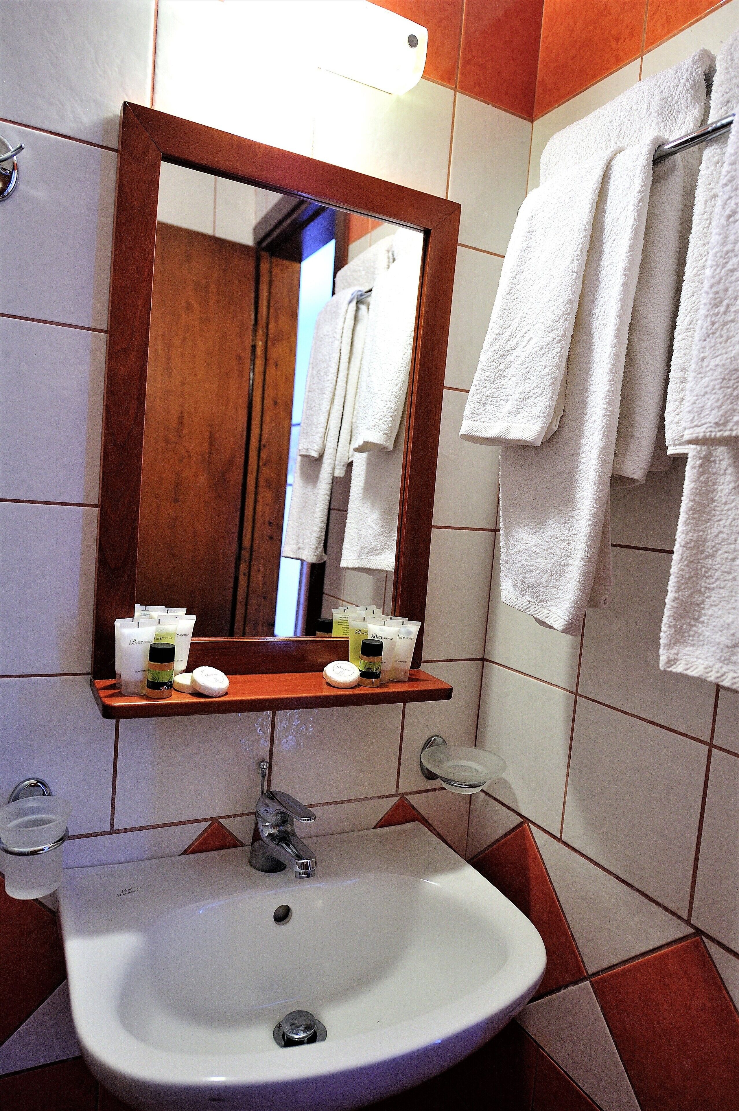 A bathroom with a white sink, a wooden-framed mirror, and a towel rack with white towels.