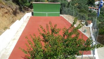 A tennis court with a green and red surface, surrounded by a white fence and trees.