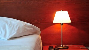 A bed with white linens and a nightstand with a lamp and remote controls. - Eye Q Resort (Skiathos)