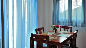 A dining area with a wooden table, four chairs, a vase with flowers, and blue curtains. - Eye Q Resort (Skiathos)