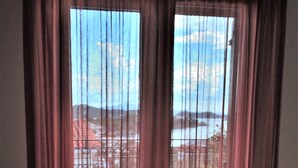 A room with a large window covered by sheer curtains, offering a view of a balcony with outdoor furniture. - Eye Q Resort (Skiathos)